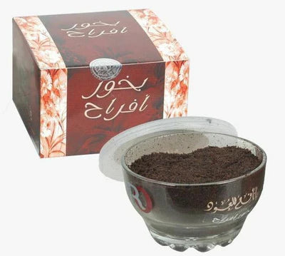 A glass jar filled with brown bakhoor powder, placed in front of its packaging box which has Arabic script from Malik Foodstore